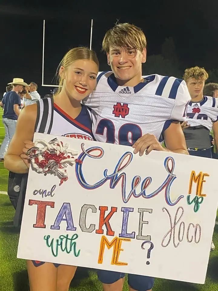 two people holding a sign that says cheer me tackle up with me on the sidelines