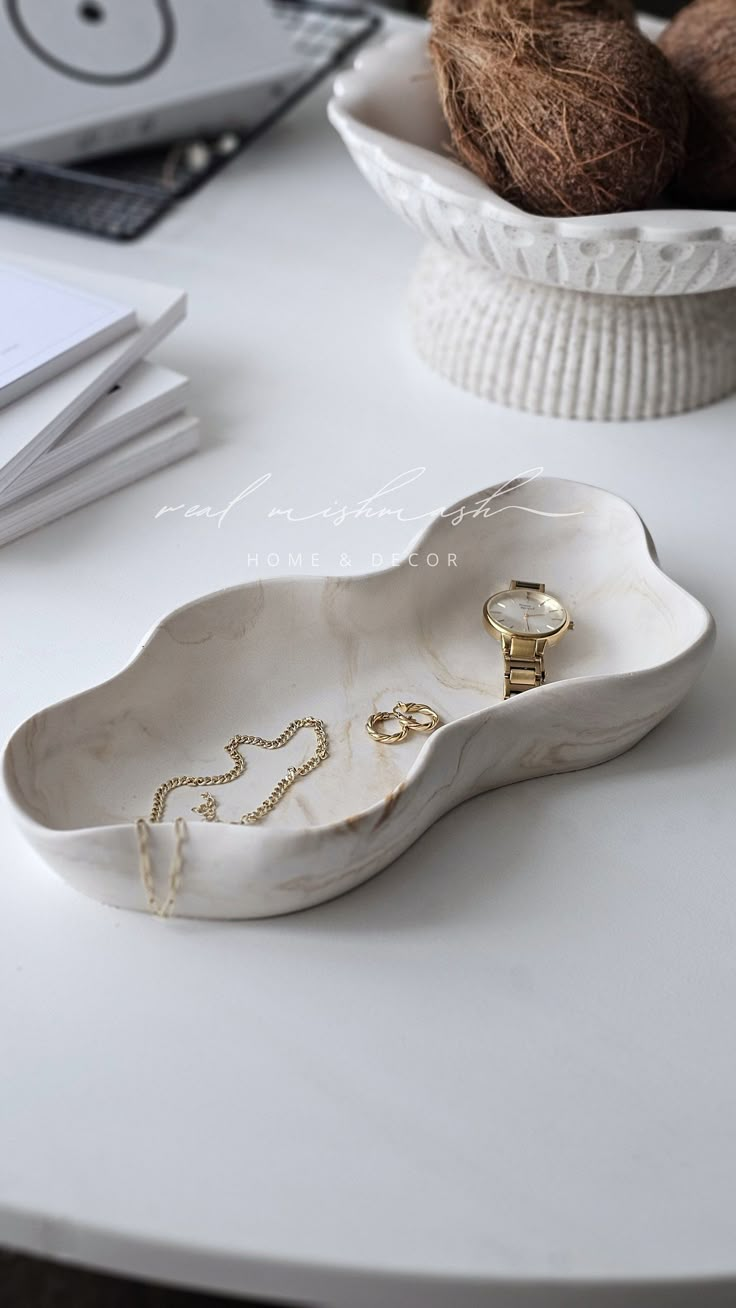 a white table topped with a bowl filled with fruit and a gold ring sitting on top of it