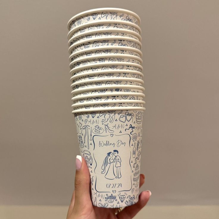 a hand holding up a stack of paper cups with drawings on the bottom and sides