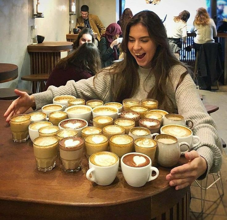 a woman sitting at a table with many cups of coffee in front of her and smiling