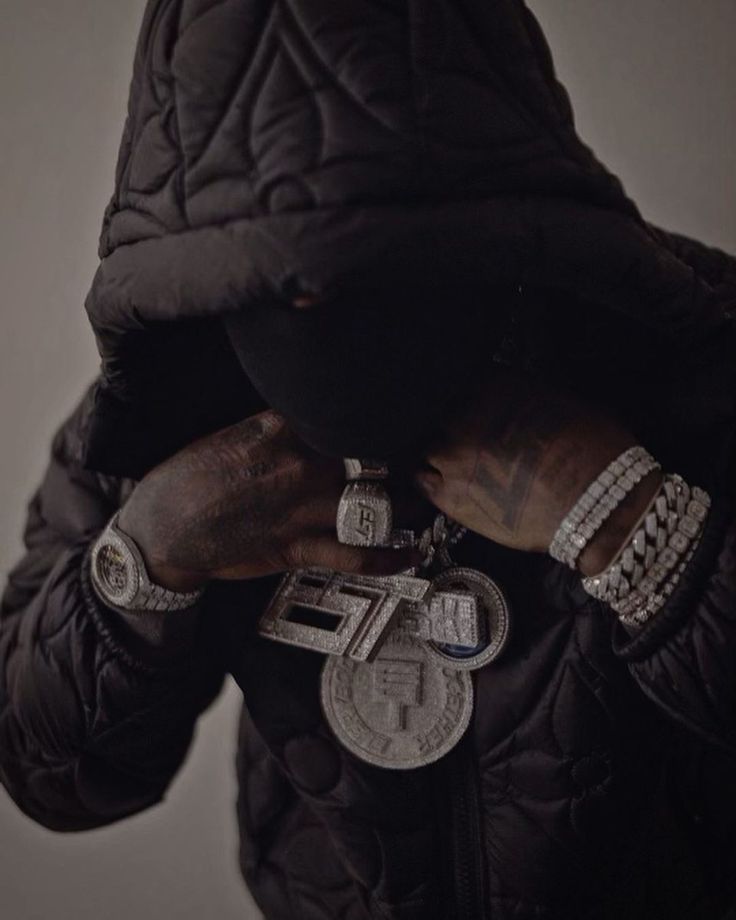 a man in a black jacket with his hands on his face and two chains around his neck