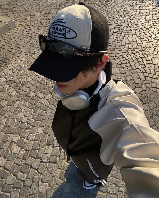 a young boy wearing headphones and a baseball cap is standing on a cobblestone street