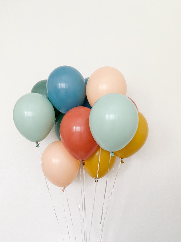 a bunch of balloons floating in the air on top of a white wall with string