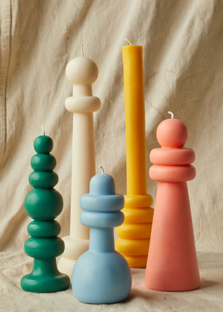 candles are lined up next to each other on a white cloth covered surface, with one lit candle in the middle