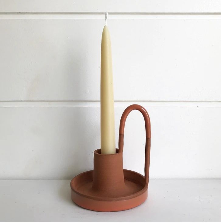 a candle sits in a clay holder on a white surface with a wall behind it