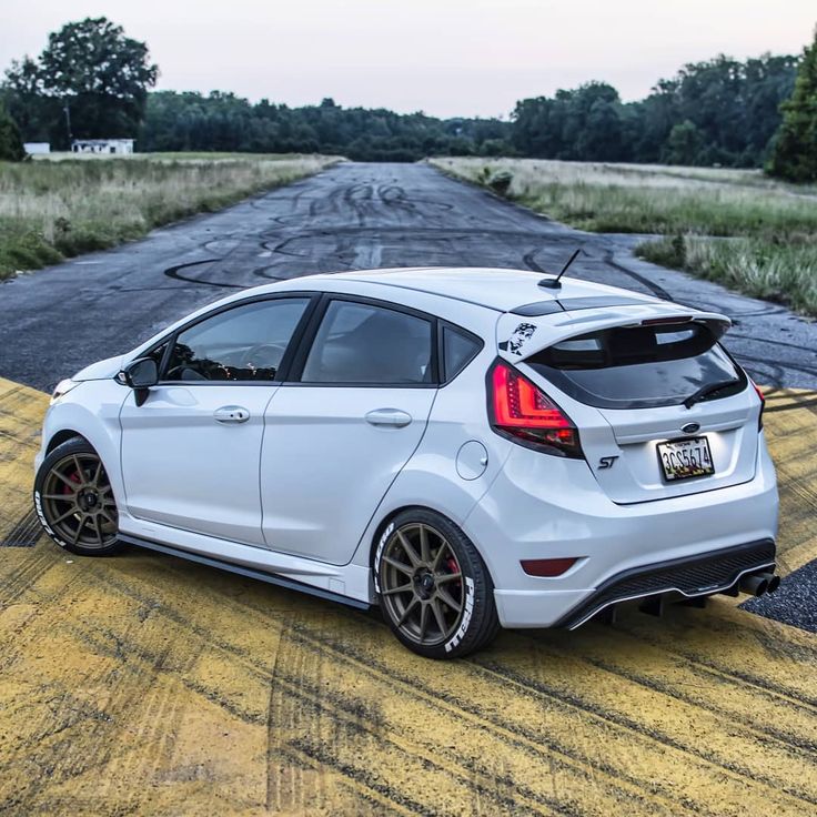 the rear end of a white ford focus st on a road with trees in the background