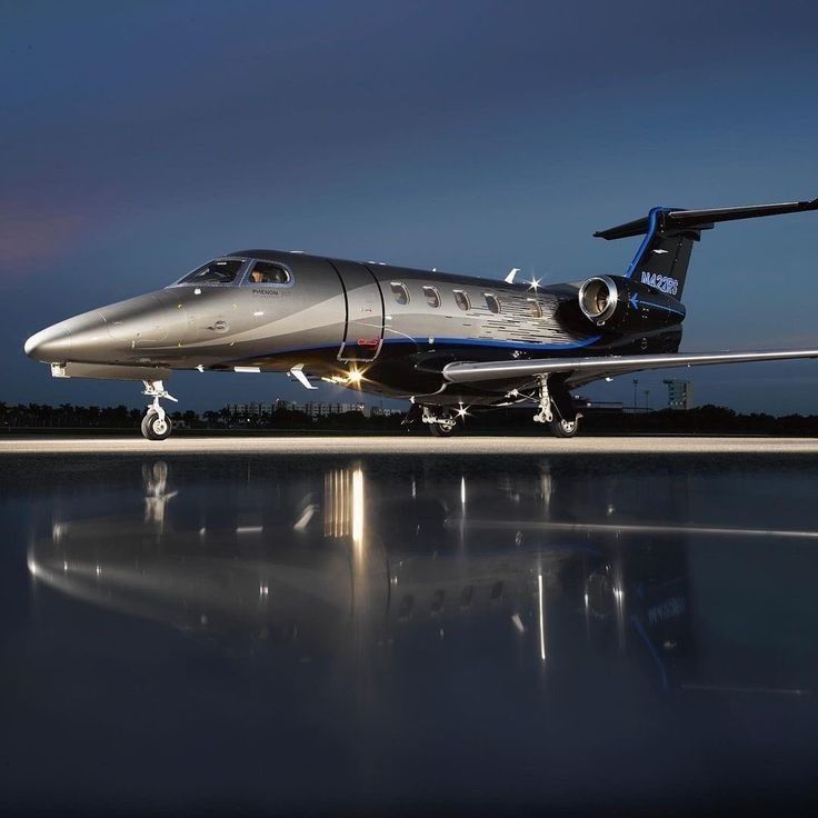 a silver and blue jet sitting on top of an airport tarmac at night with its landing gear down