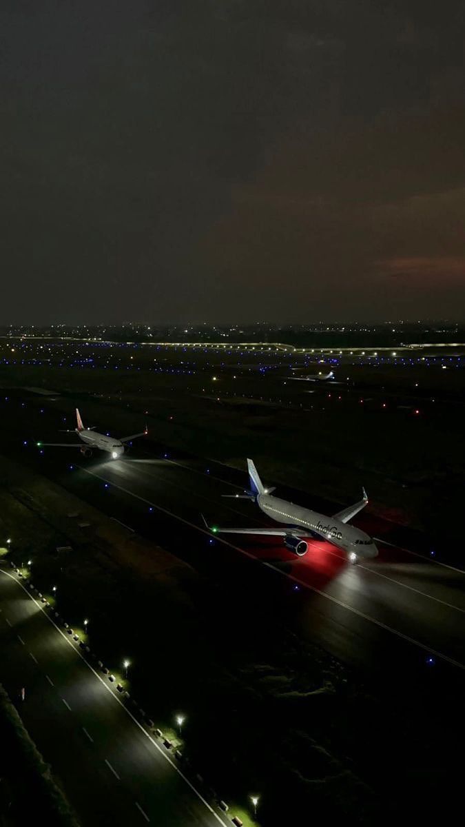 an airplane taking off at night with lights on the ground and in the background, there is a runway