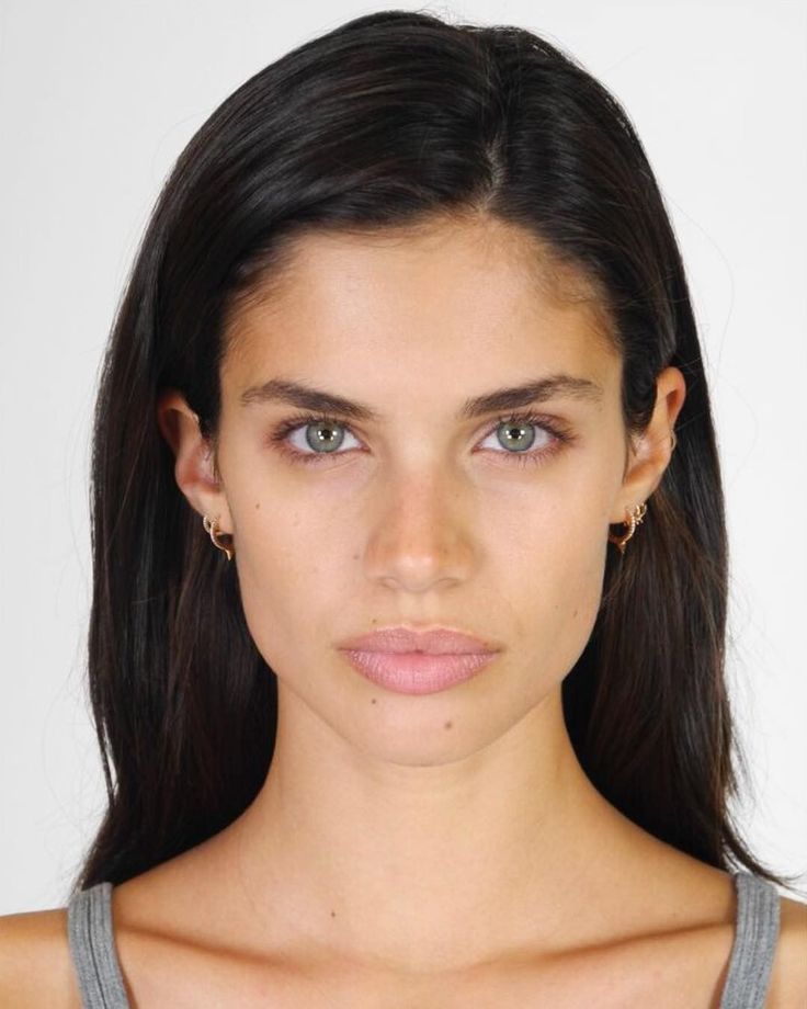 a young woman with blue eyes and long dark hair is looking at the camera while wearing a gray tank top