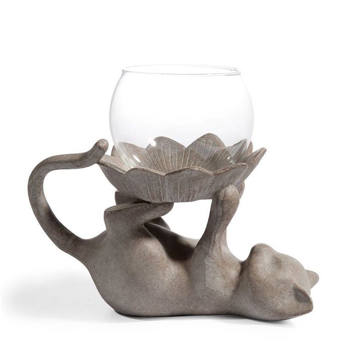 a glass bowl sitting on the back of a cat with its legs in it's mouth