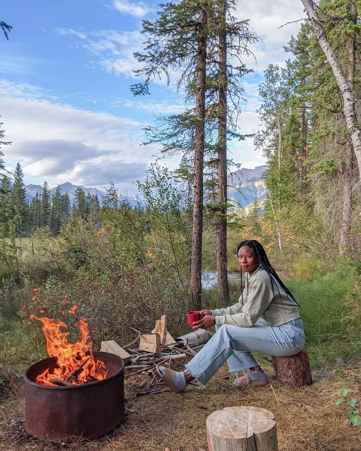 a woman sitting next to a campfire in the woods