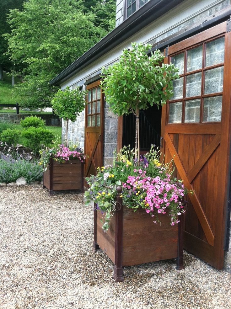 two wooden planters filled with flowers next to a barn door on graveled ground