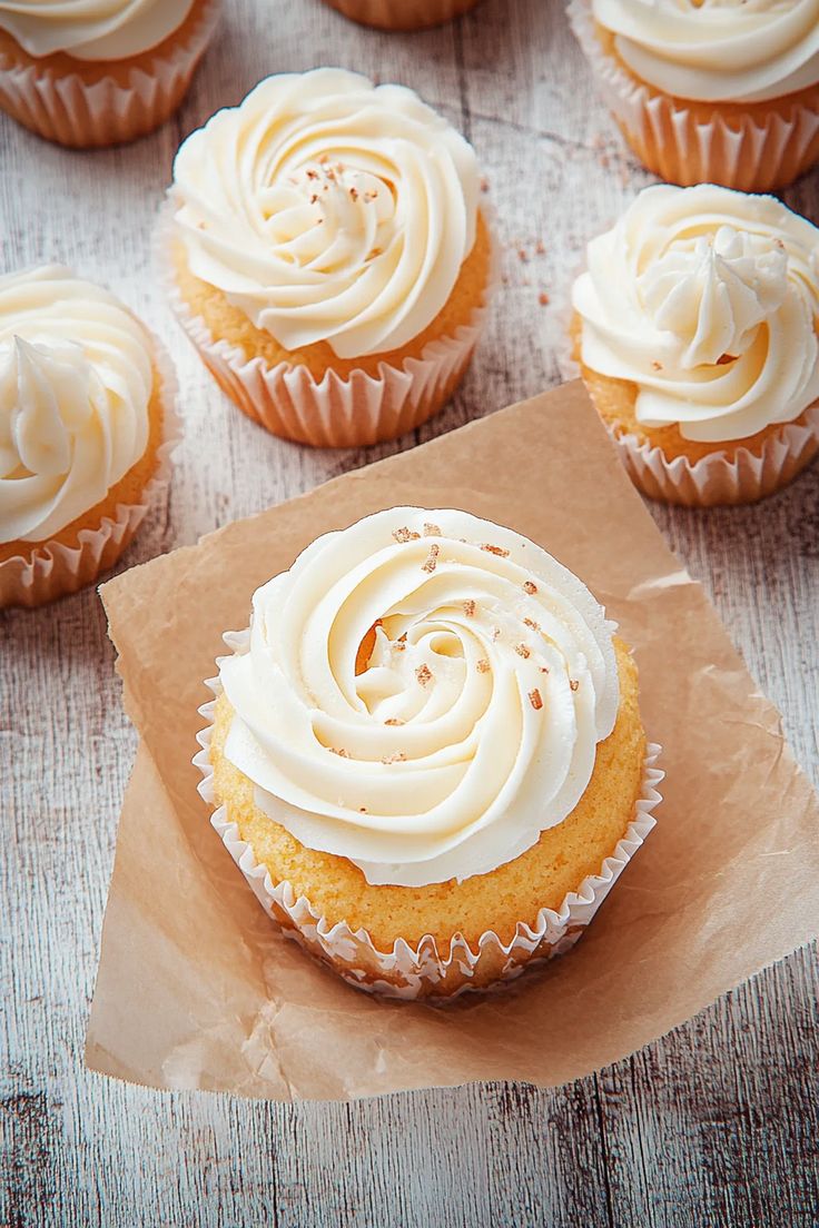 cupcakes with white frosting and sprinkles sitting on brown paper