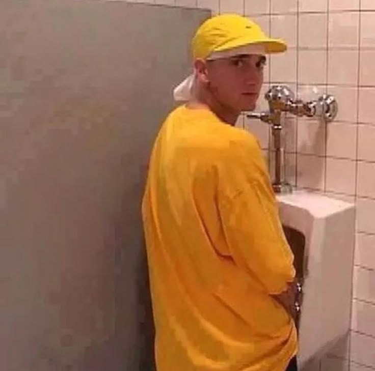 a man wearing a yellow hat standing next to a urinal