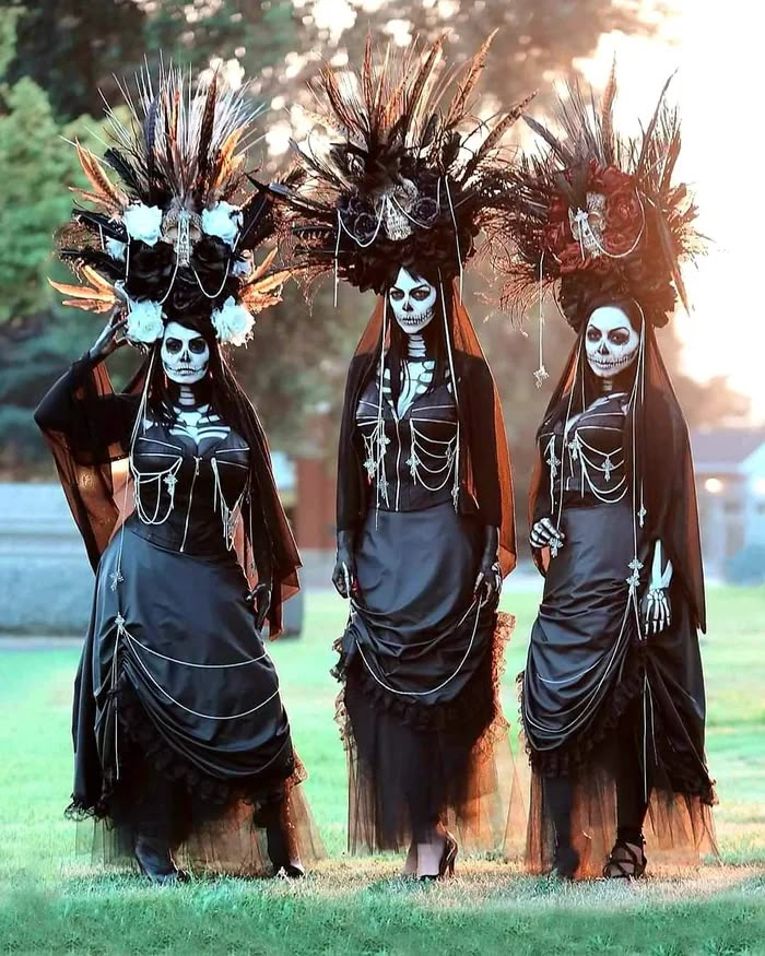 three women dressed in skeleton costumes standing next to each other on a grass covered field