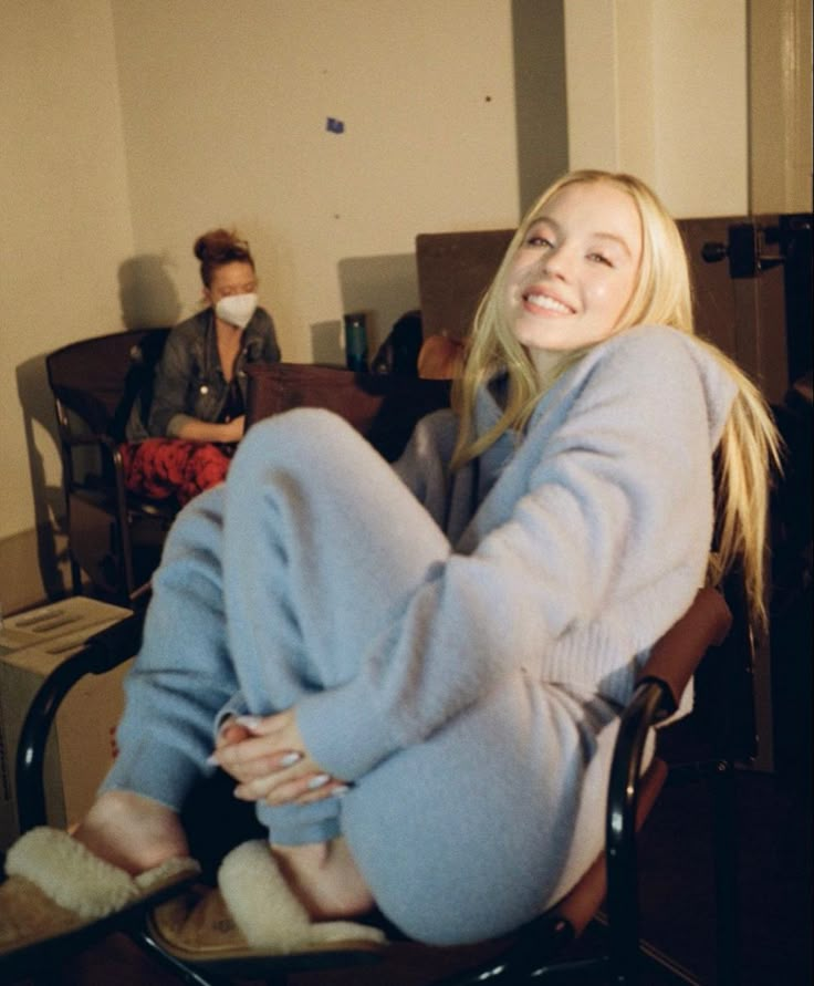 a blonde woman sitting in a chair with her legs crossed and smiling at the camera