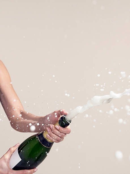 a woman holding a bottle of champagne and spraying it on her face with water droplets