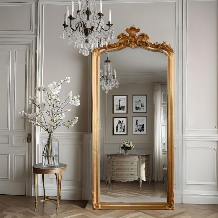 a large gold framed mirror sitting in a living room next to a vase with flowers