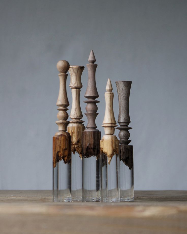 four glass vases with wooden posts in them on a table next to each other