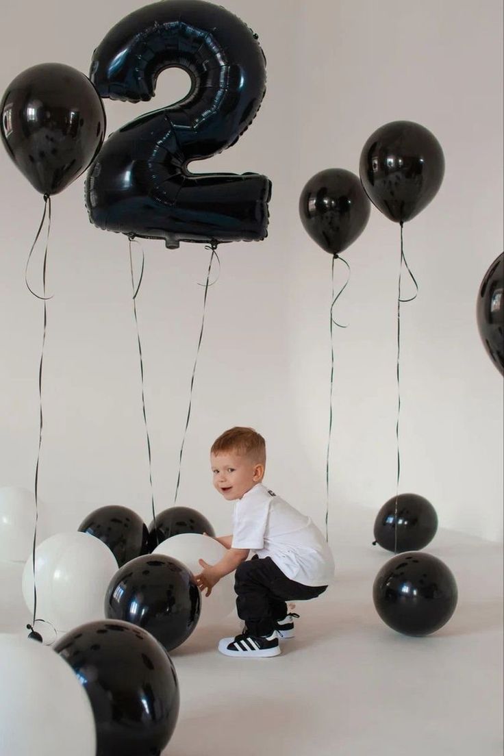 a young boy kneeling down in front of balloons with the number two on them and one balloon