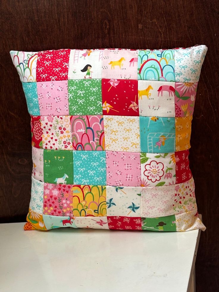 a colorful patchwork pillow sitting on top of a white table next to a wooden wall