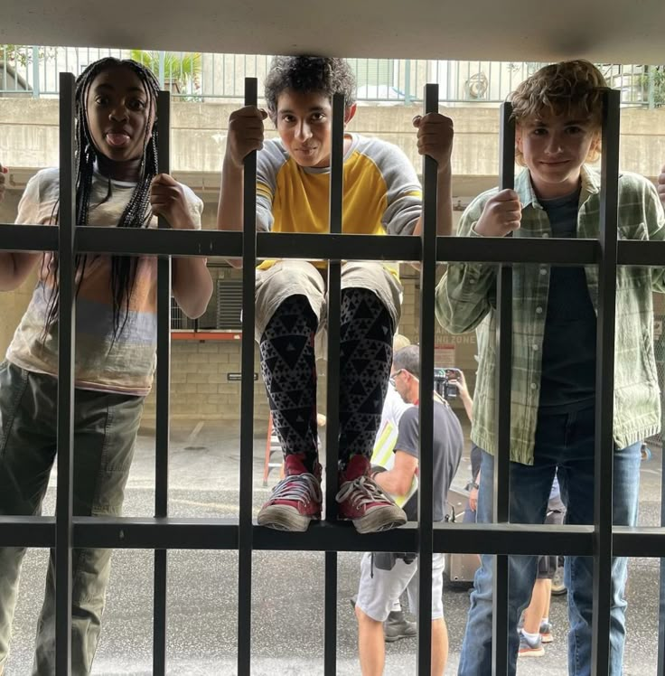 three boys behind bars in a jail cell with one boy holding on to the bars