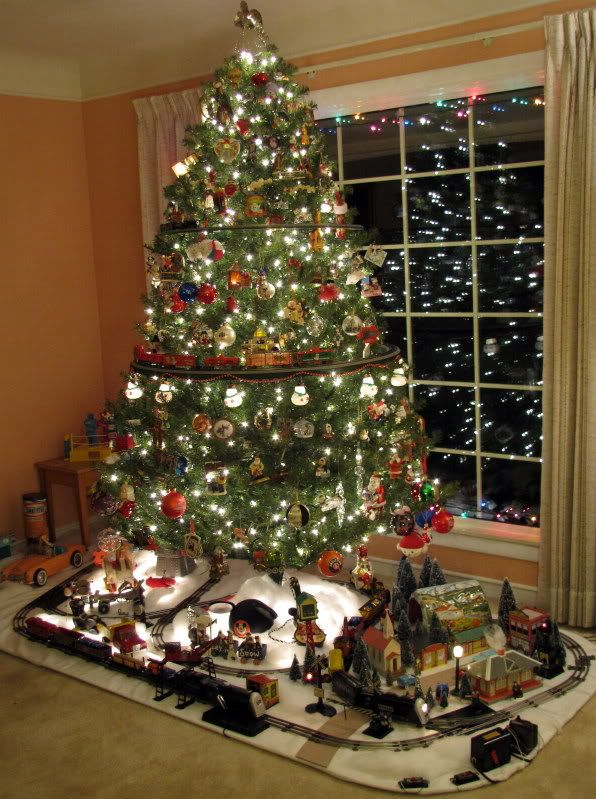 a christmas tree in the corner of a living room with lights on and presents under it