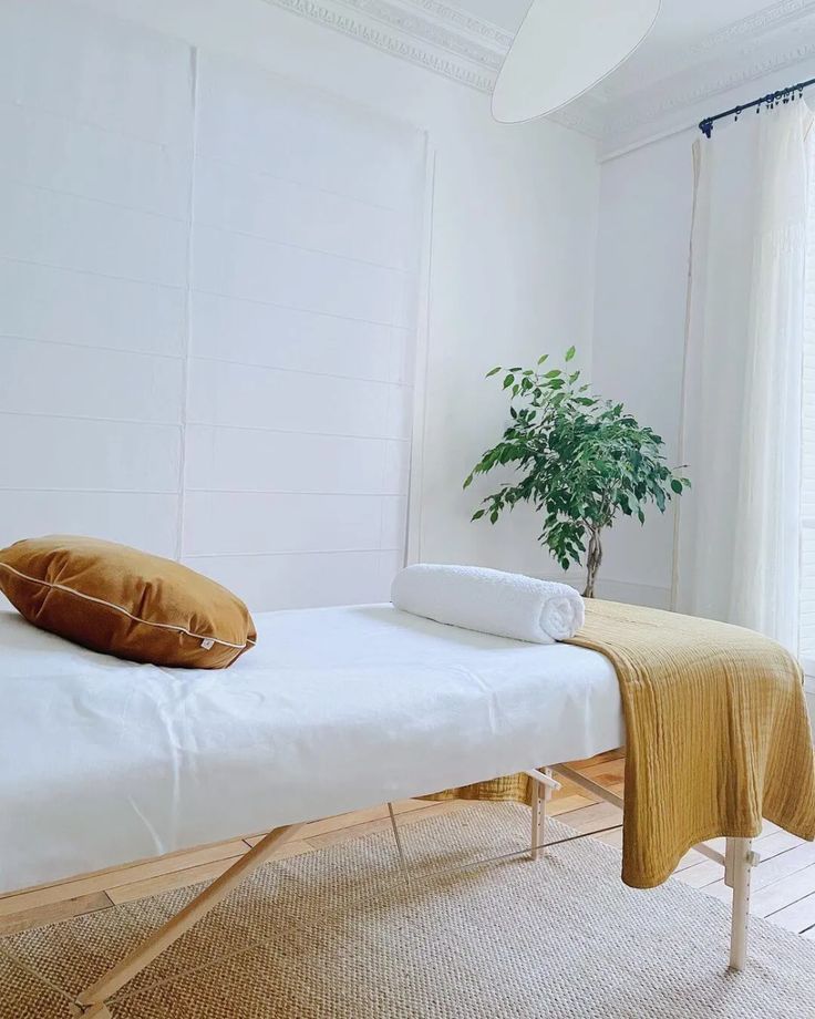 a white bed sitting in a bedroom next to a plant on top of a table