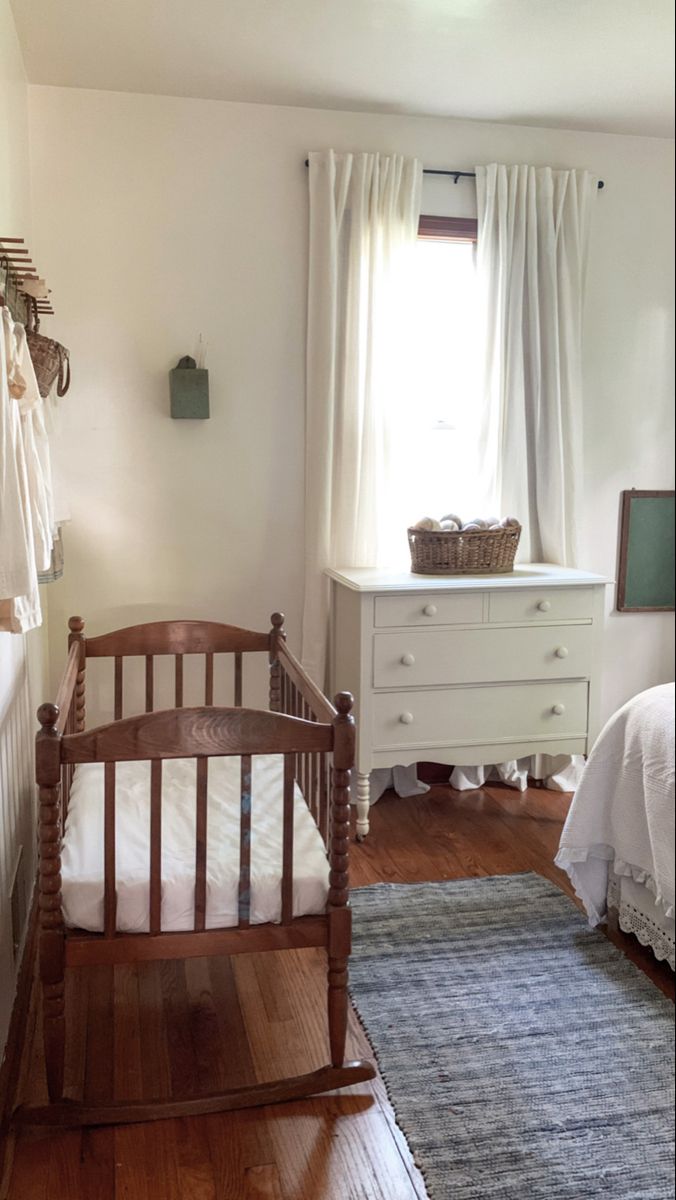 a baby's crib in the corner of a room with white walls and wooden floors