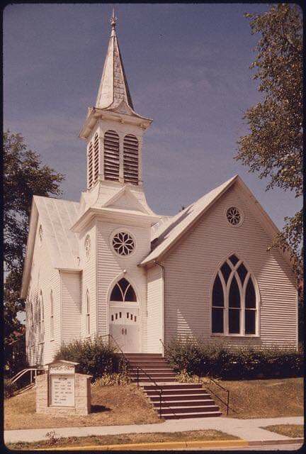 an old church with stairs leading up to the front door and steeple on a sunny day