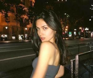 a beautiful young woman standing on top of a balcony next to a street at night