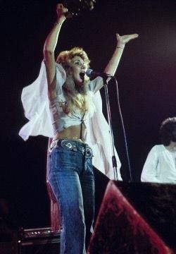 a woman standing on top of a stage with her arms in the air and singing into a microphone