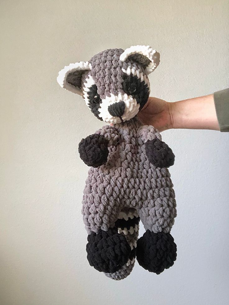 a crocheted raccoon stuffed animal being held by someone's hand