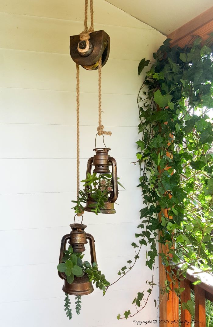 two hanging lanterns with plants growing on the side of a house next to a porch