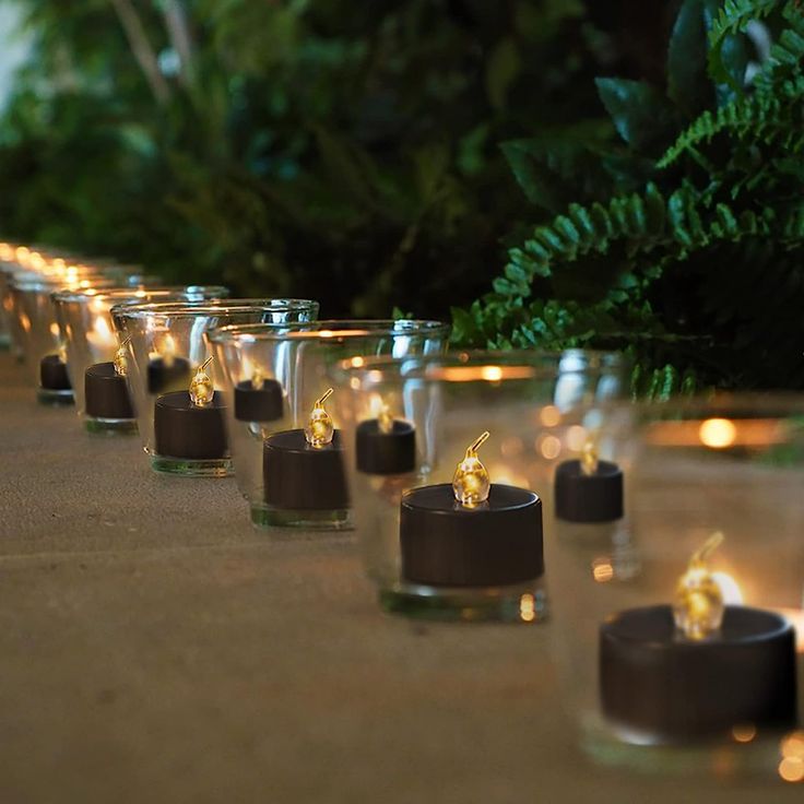 there are many small glass candles lined up on the table with some lights in them