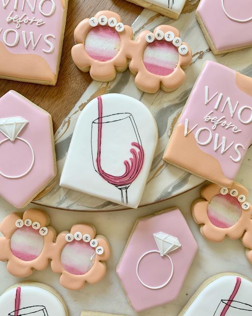 decorated cookies with pink and white icing on a table next to some wine glasses