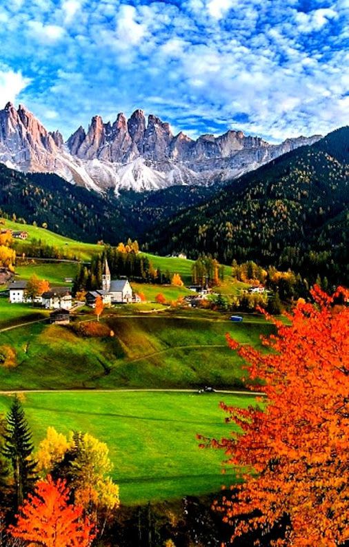 the mountains are covered in colorful trees and green grass, with houses on each side