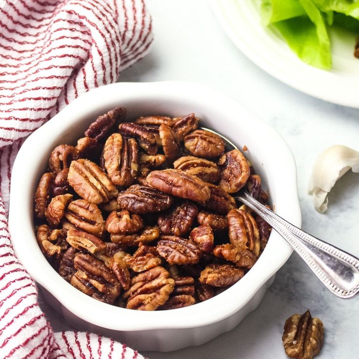 a white bowl filled with pecans next to a plate of lettuce