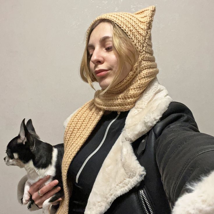 a woman holding a small black and white dog wearing a knitted hat on top of her head