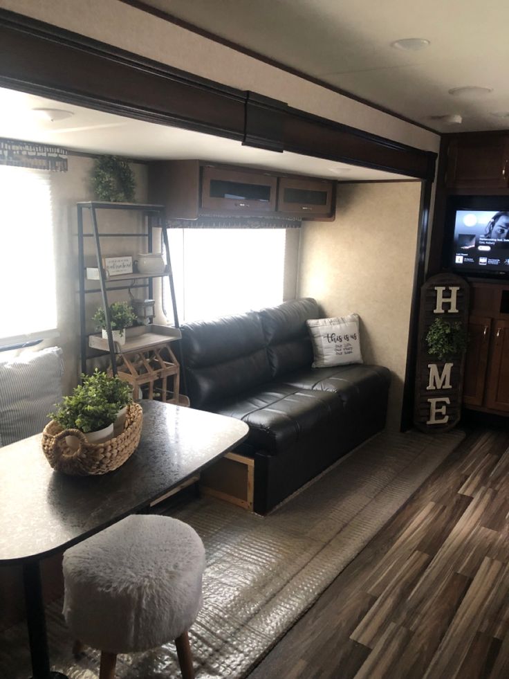 a living room and dining area in a recreational vehicle with wood floors, black leather couch