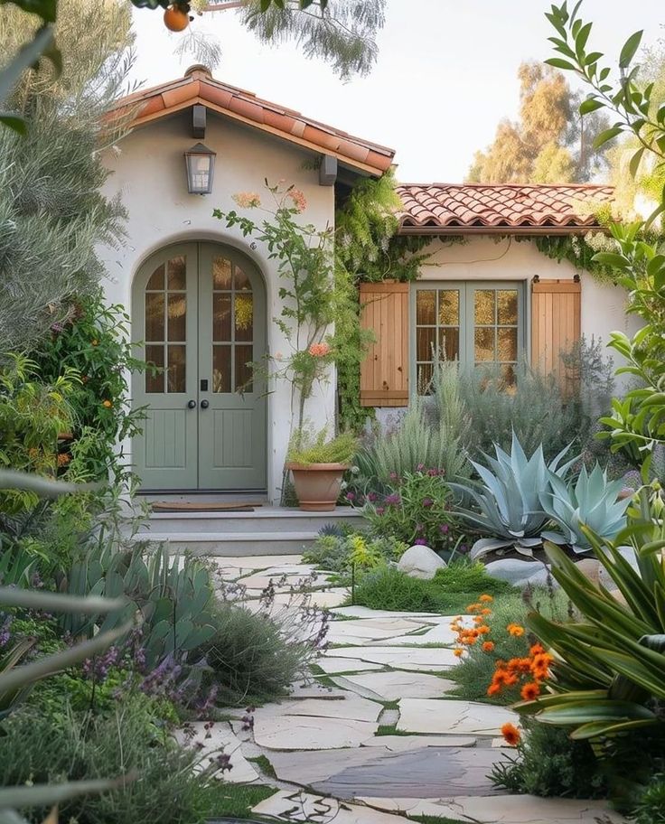 a house that is surrounded by plants and flowers in front of the entrance to it