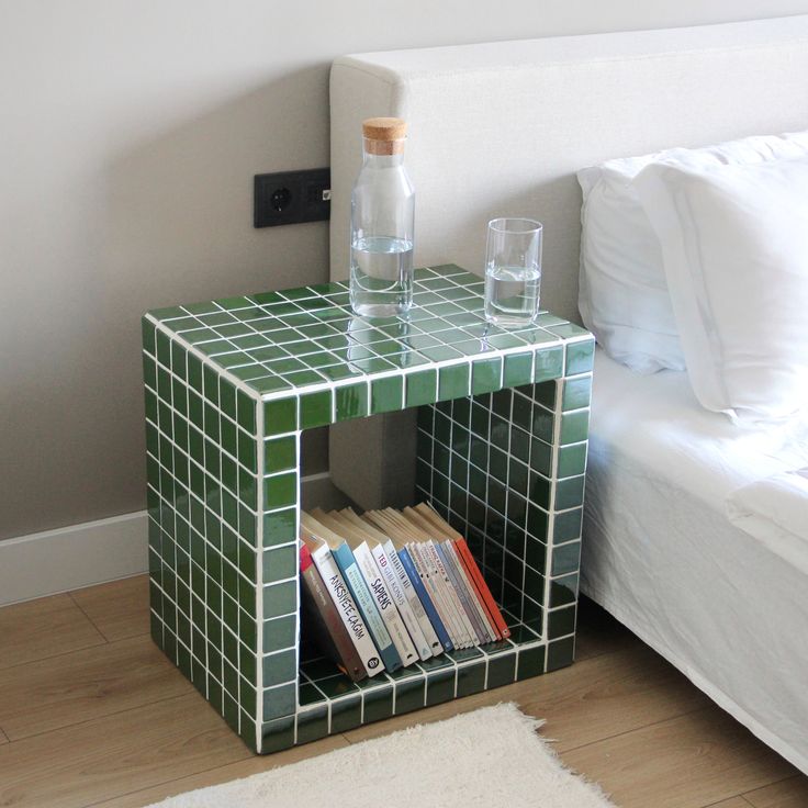 a green tiled side table with two glasses on top and books in front of it