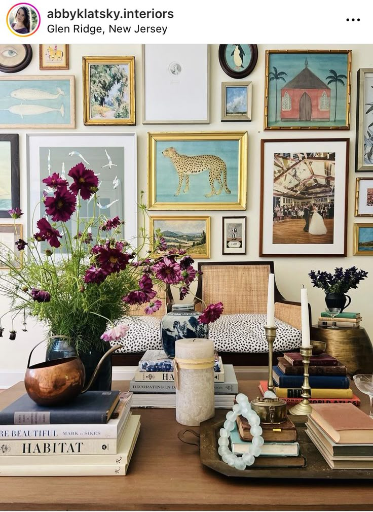 a table topped with books and vases filled with flowers next to pictures on the wall