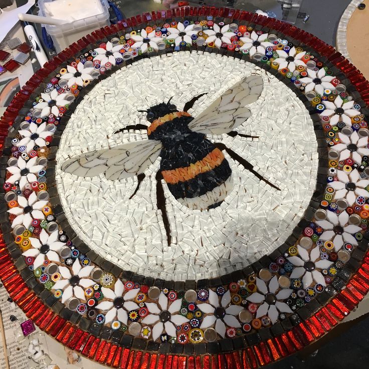 a mosaic with a bee on it sitting on top of a table next to other items