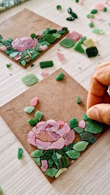 a person is making mosaics with green and pink flowers on brown paper that are scattered around them