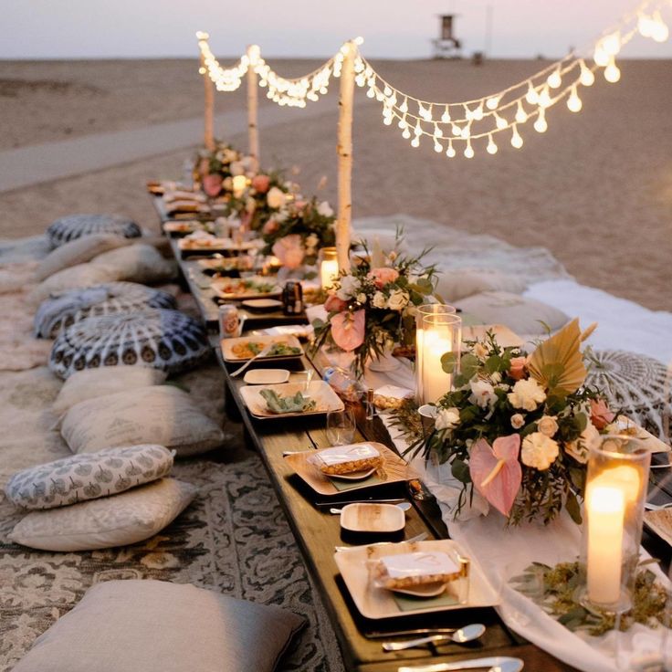 a long table is set up on the beach with candles, plates and napkins