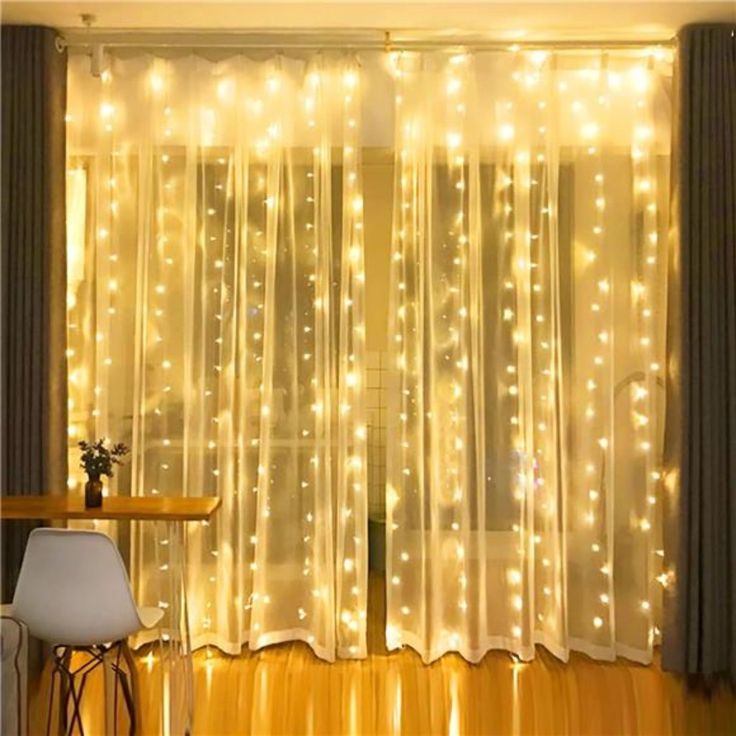 curtains with lights on them are hanging in front of a table and chair near a window