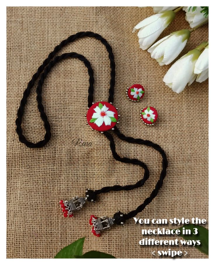 a necklace and earring set with flowers on black cord, sitting next to tulips