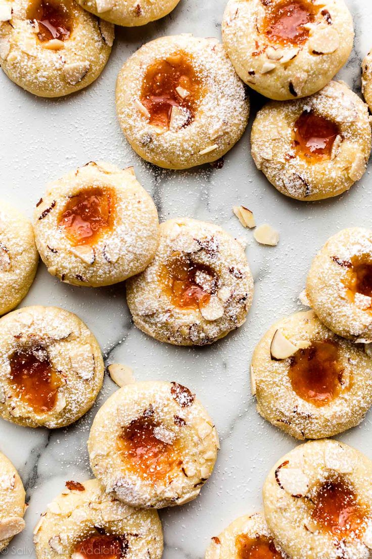 powdered sugar and jelly cookies on a marble counter top, with almonds scattered around them