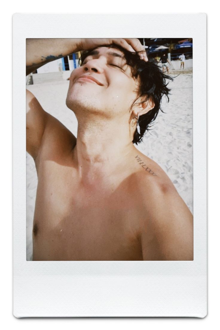 a shirtless man on the beach with his head in his hands and eyes closed